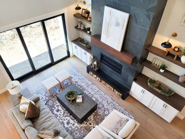 Hardwood flooring, stone-clad fireplace with wood mantle, built-in cabinetry with wood-finish countertops, and large sliding glass doors