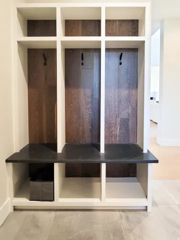 Built-in mudroom cubbies with dark wood-finish backing, a dark countertop, integrated hanging hooks, and lower storage compartments