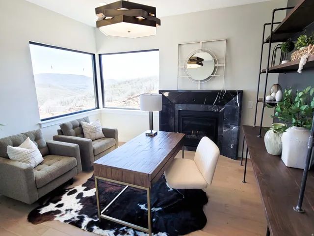 Corner windows, gas fireplace with black stone surround, wood-finish flooring, built-in shelving, and contemporary light fixture
