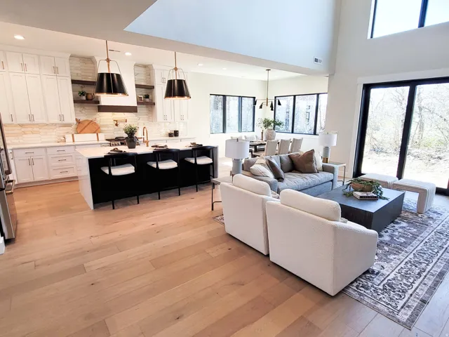 Open-concept living space featuring wood-finish flooring, a kitchen island with seating, white shaker cabinetry, and a double-height ceiling