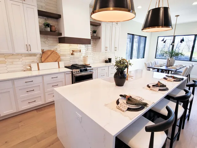 Spacious kitchen featuring an expansive island with seating, light wood-finish flooring, white cabinetry, a built-in oven range, and a patterned backsplash