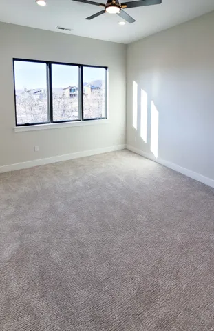 Expansive room featuring plush wall-to-wall carpeting, a multi-pane window with black trim, a ceiling fan with integrated lighting, recessed lighting, and crisp white trim