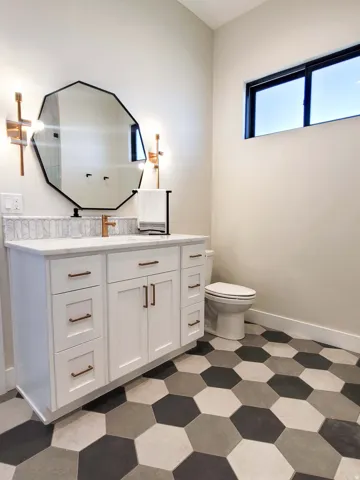 White vanity with bronze hardware, a contrasting geometric mirror, and a mosaic tile backsplash