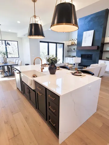 Kitchen island with a waterfall countertop, farmhouse sink, and bronze faucet