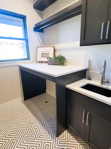 Geometric pattern tile flooring, dark cabinetry with brushed nickel hardware, white countertop, stainless steel sink with a gooseneck faucet, and integrated open shelving