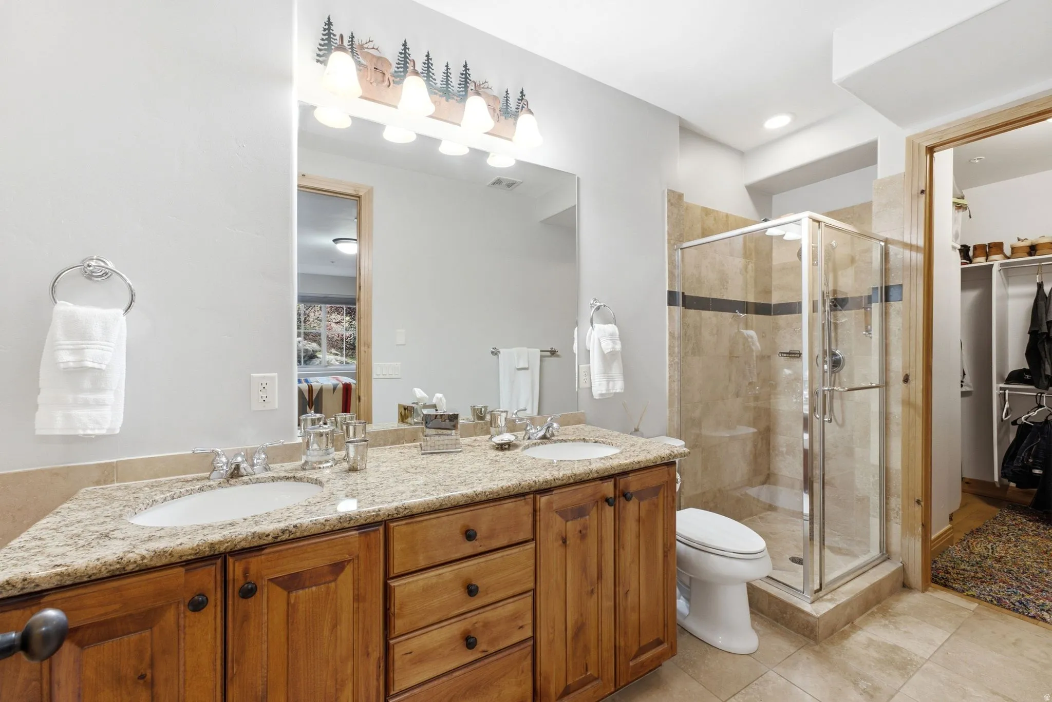 Dual vanity granite countertop, tile flooring, glass-enclosed shower, and wood cabinetry