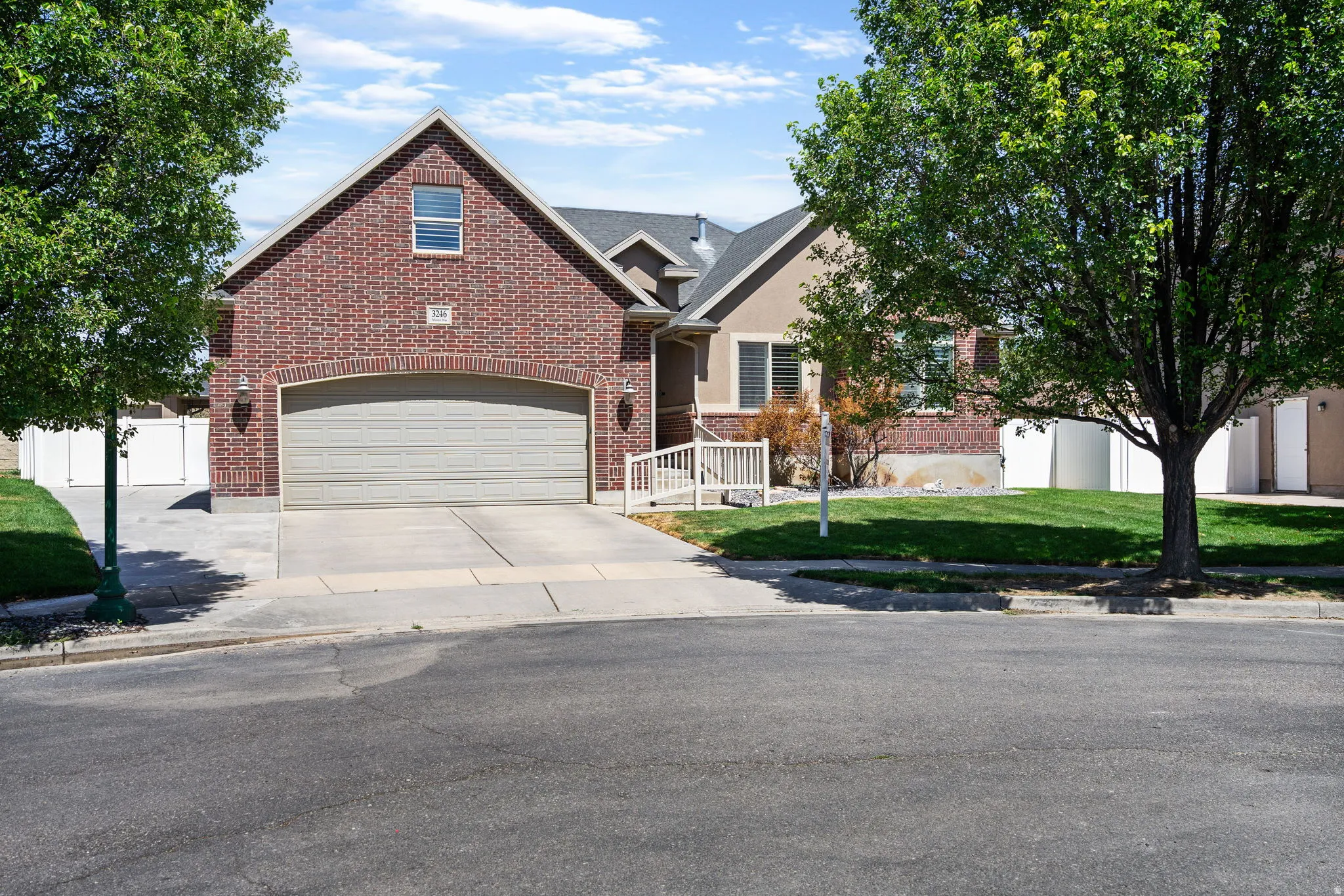 Brick facade with stucco accents, an attached garage, a concrete driveway, and a white fence