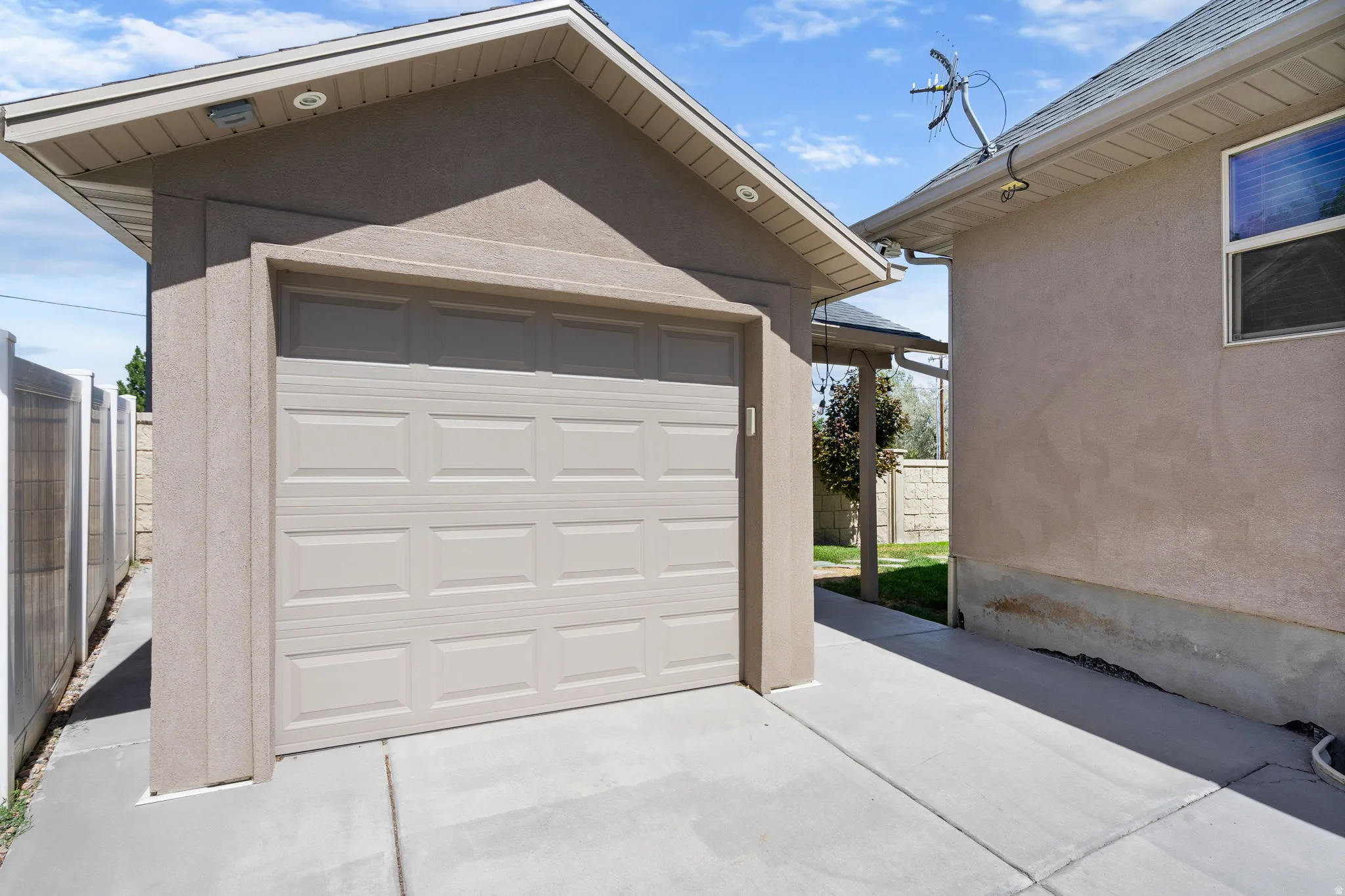 Detached garage with a paneled door, concrete driveway, stucco exterior, and soffit lighting