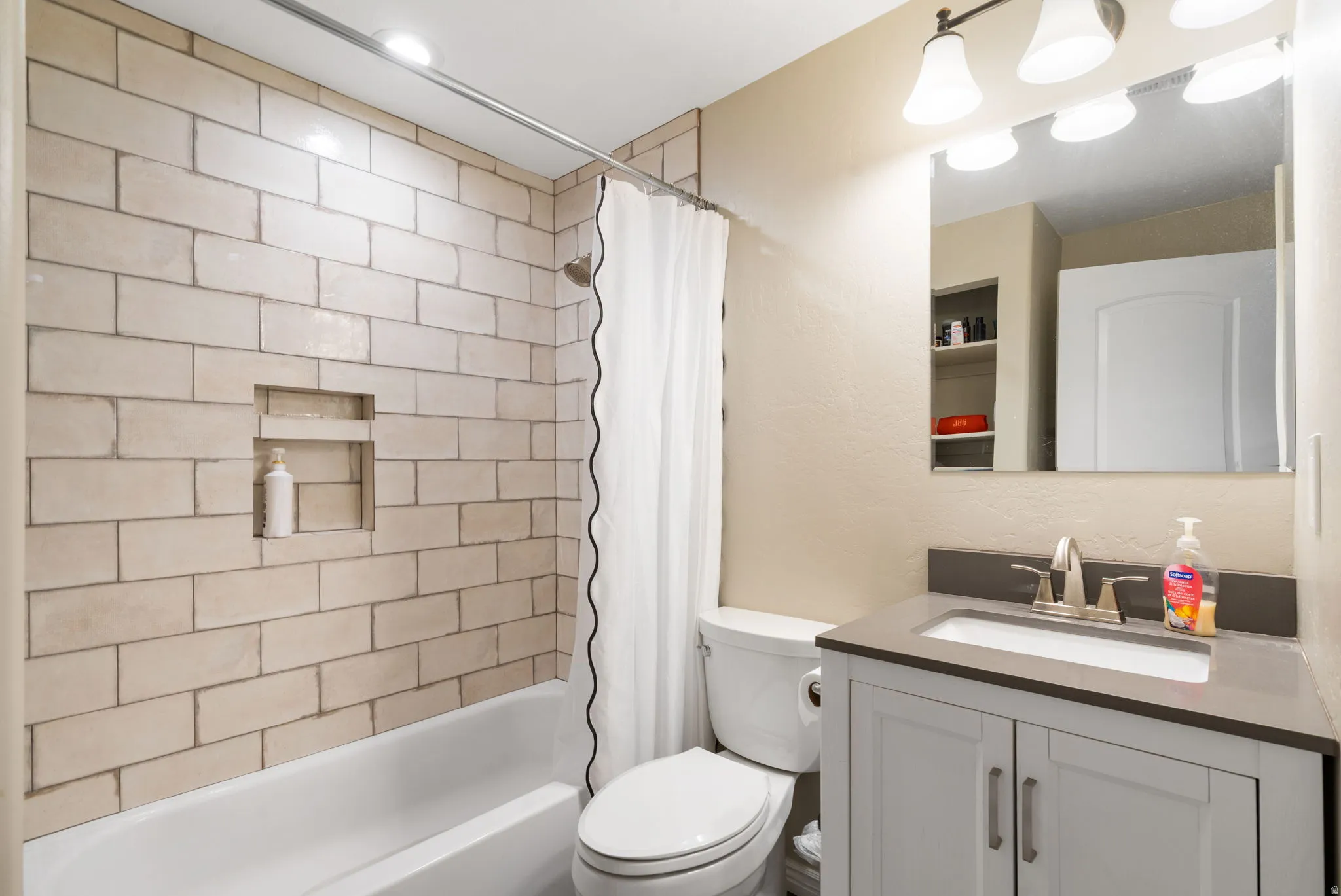 Bathtub with subway tile surround, recessed shower niche, single vanity with undermount sink, and wall-mounted mirror