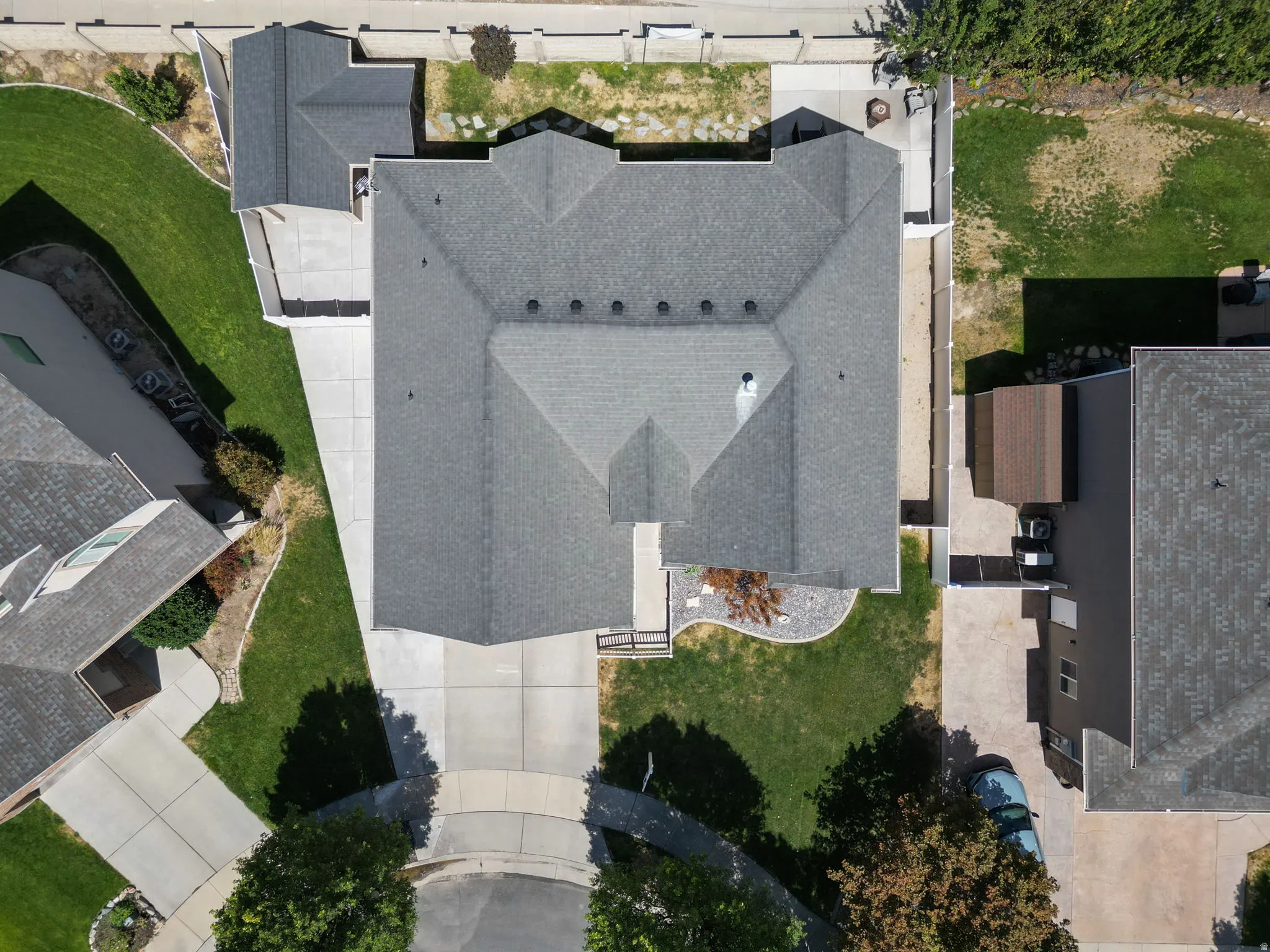 Gable roofline, gray shingle roofing, paved driveway, landscaped front yard, paved patio area