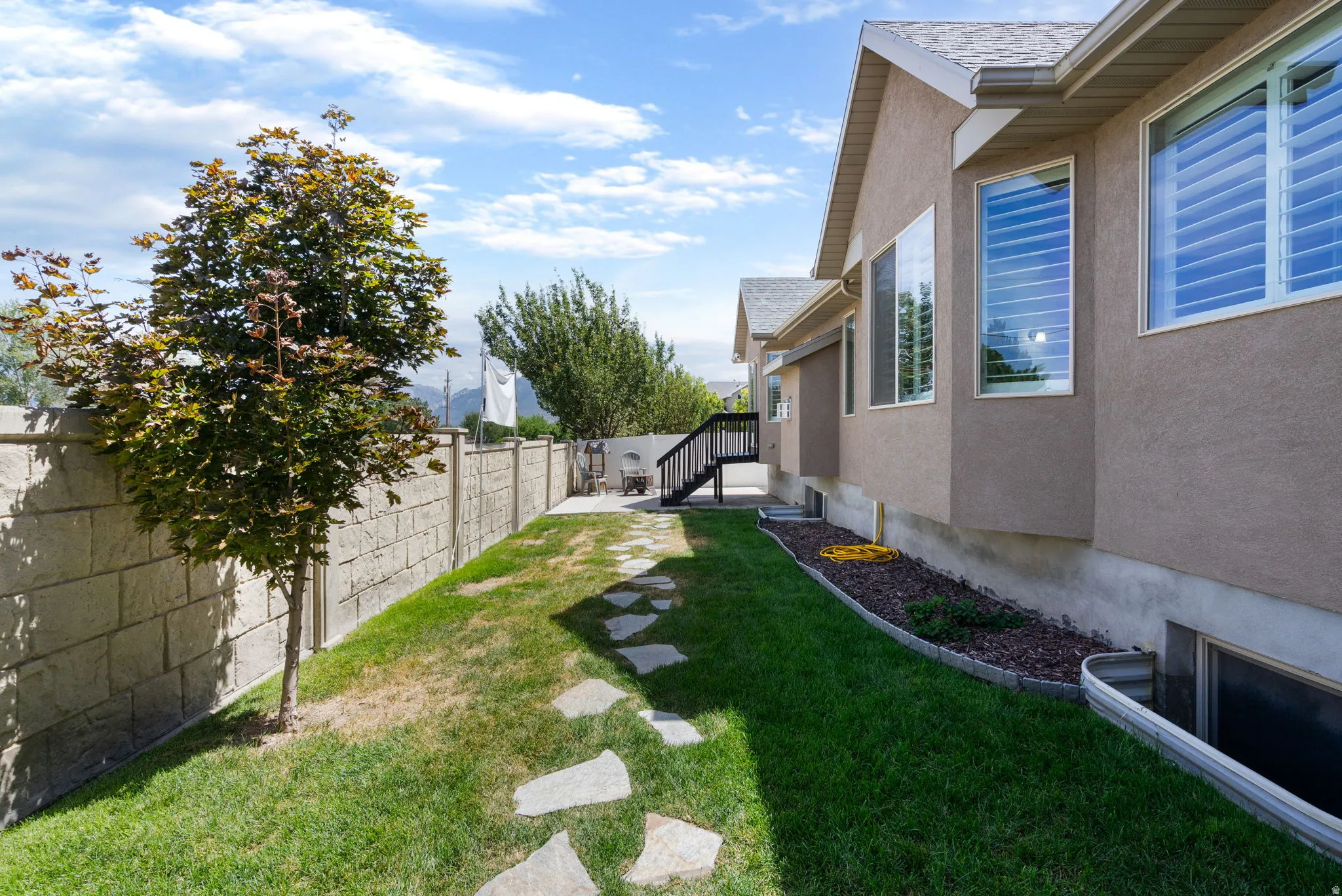Expansive lawn with a stone block privacy wall, mature tree, and stepping stone pathway