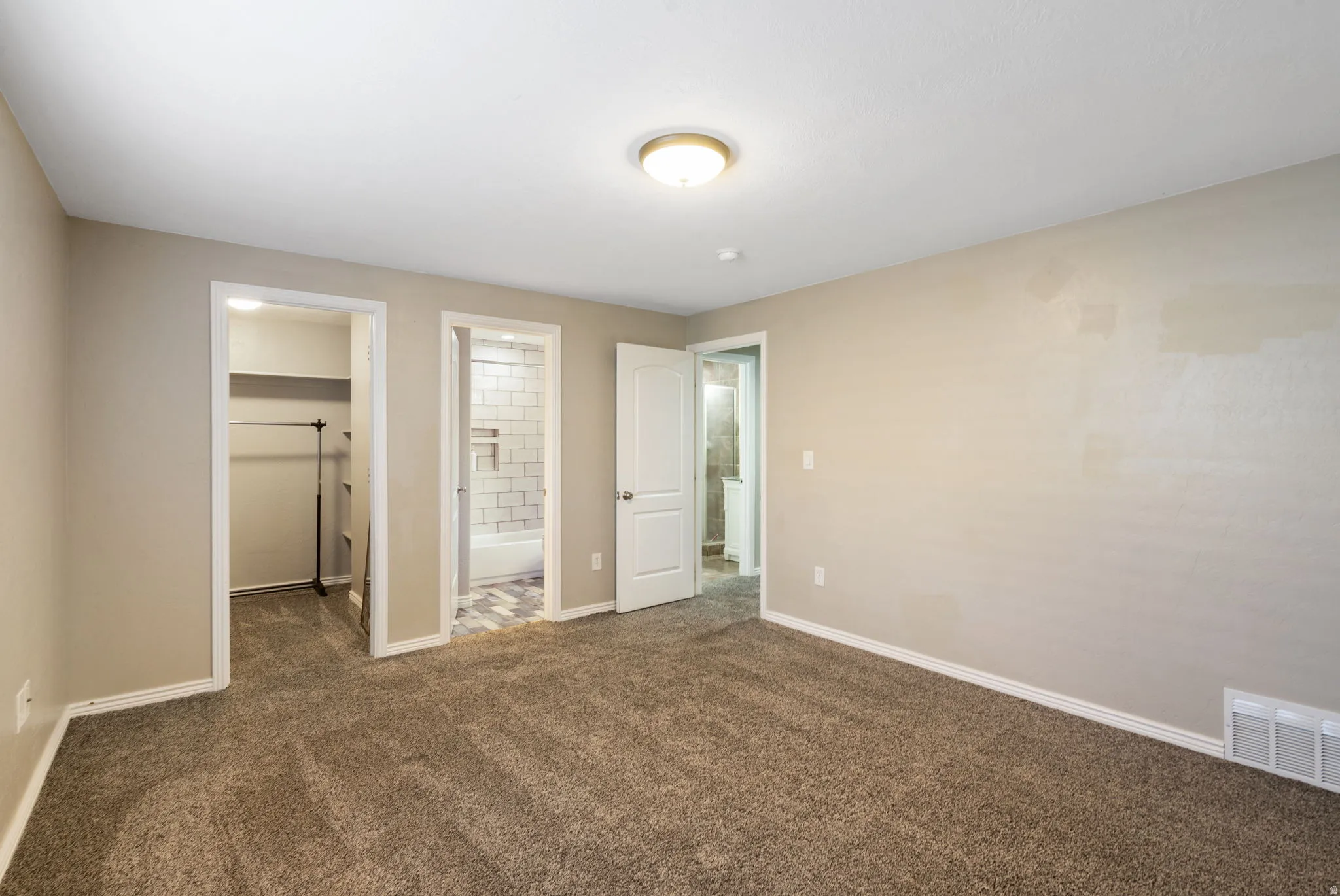 Plush carpet flooring, neutral painted walls, recessed closet shelving, and a bright overhead light fixture