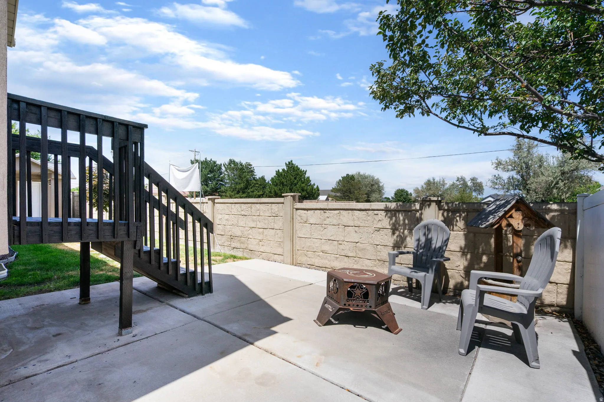 Concrete patio with a dark wood deck and stairs, complemented by a block retaining wall