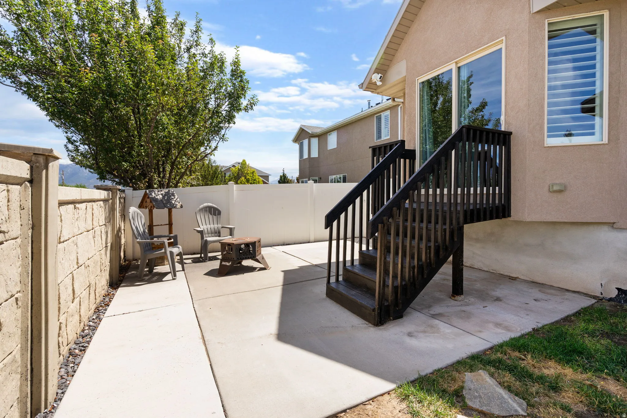 Ground-level concrete patio with direct access to an upper-level deck featuring dark wood stairs and railings