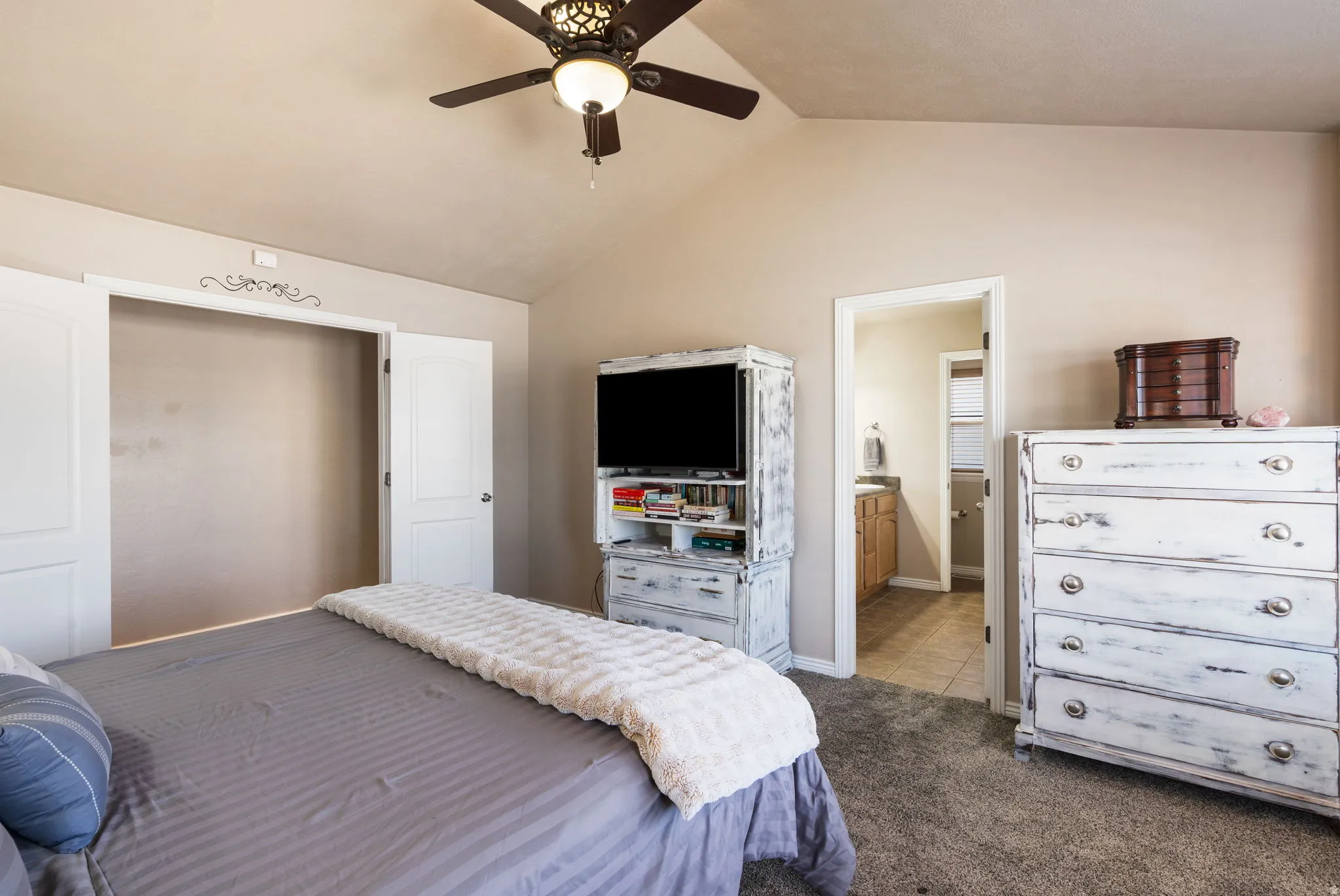 Vaulted ceiling, ceiling fan with integrated lighting, built-in closet with double doors, neutral-toned carpeting, and a full bathroom with a single vanity
