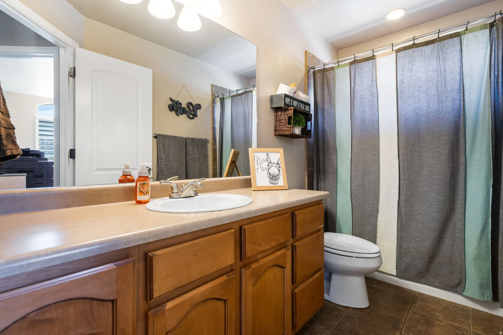 Bathroom featuring a wood-finish vanity with an integrated sink, a large wall-mounted mirror, and a shower with an overhead light
