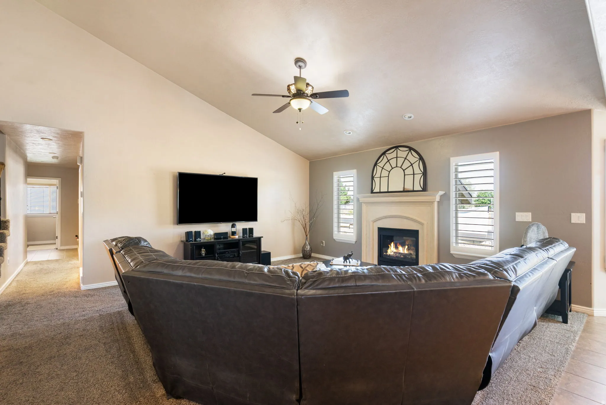 Vaulted ceiling, ceiling fan, fireplace with mantel, window shutters, and wood-finish flooring
