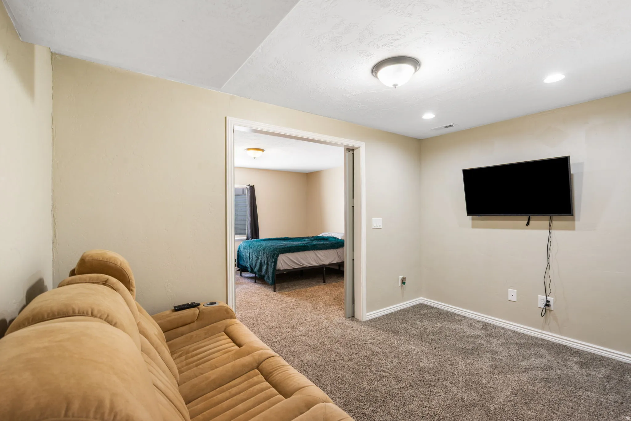 Wall-mounted television, recessed lighting, and a ceiling-mounted light fixture illuminate the carpeted floor