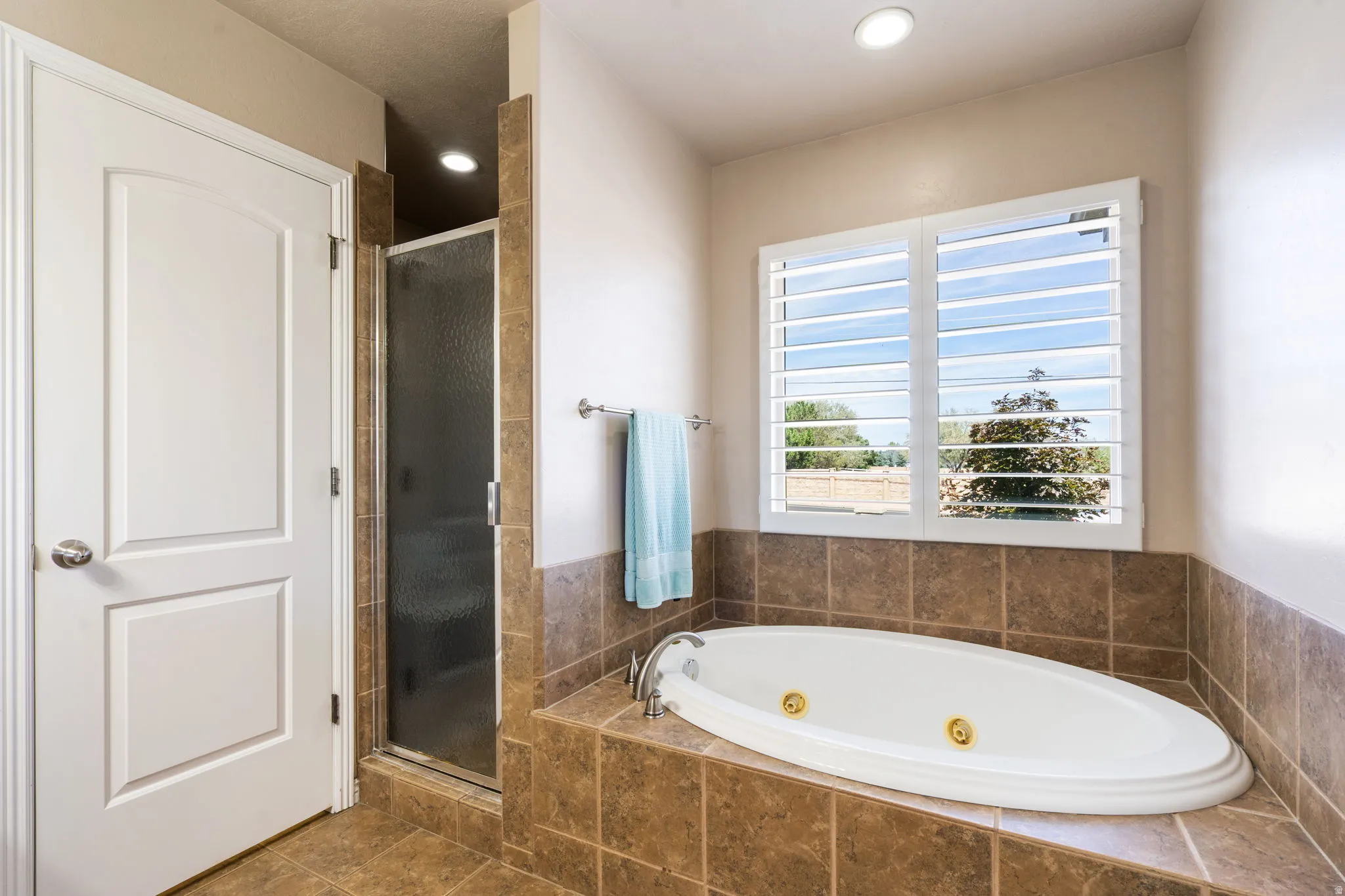 Built-in soaking tub with gold-tone fixtures, tiled surround, and plantation shutters