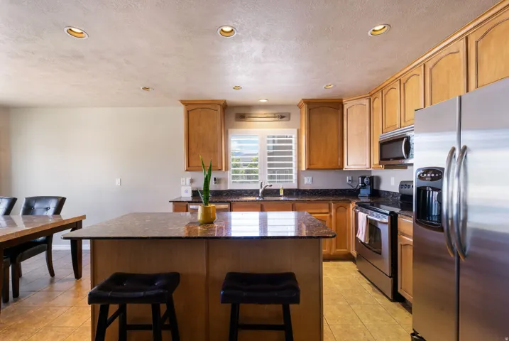 Kitchen featuring light wood cabinetry, recessed lighting, stainless steel appliances, a center island with a stone-finish countertop, and tile flooring