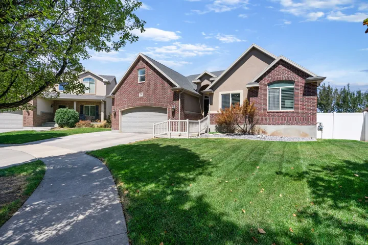 Brick Colonial featuring a professionally manicured front lawn with linear striping, mature shade trees, and a concrete driveway leading to an attached two-car garage