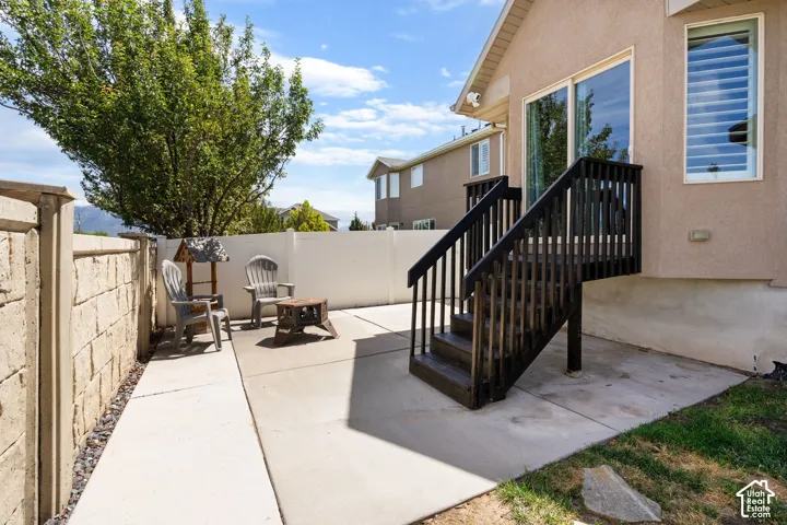 Ground-level concrete patio with direct access to an upper-level deck featuring dark wood stairs and railings