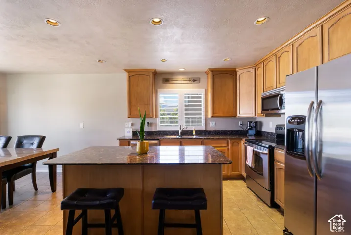 Kitchen featuring light wood cabinetry, recessed lighting, stainless steel appliances, a center island with a stone-finish countertop, and tile flooring