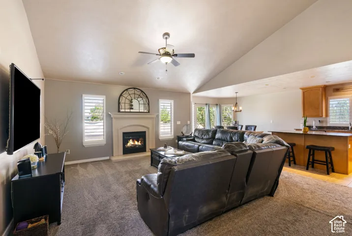 Vaulted ceiling, ceiling fan, fireplace with mantel, window shutters, and kitchen with wood-finish cabinetry