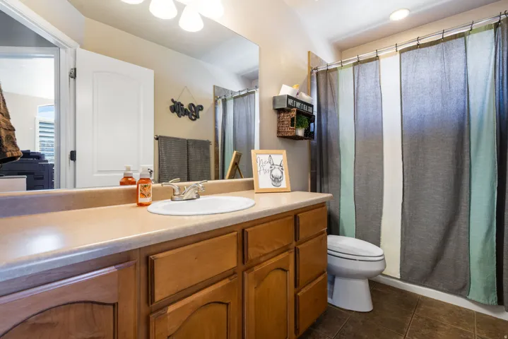 Bathroom featuring a wood-finish vanity with an integrated sink, a large wall-mounted mirror, and a shower with an overhead light