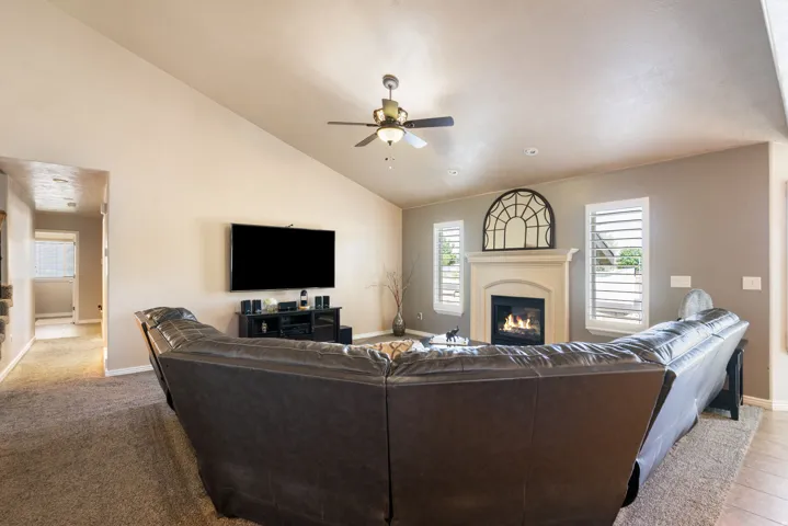 Vaulted ceiling, ceiling fan, fireplace with mantel, window shutters, and wood-finish flooring
