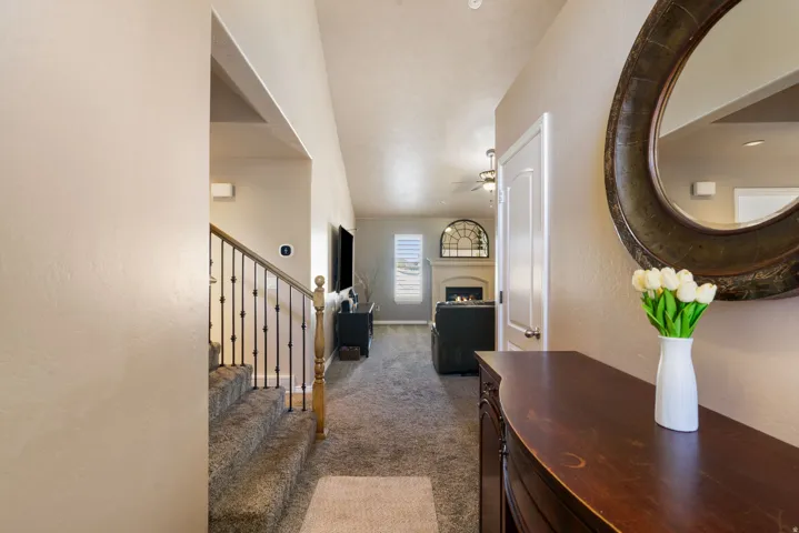 Carpeted staircase with wrought iron balusters, vaulted ceiling, and a fireplace with arched accent window