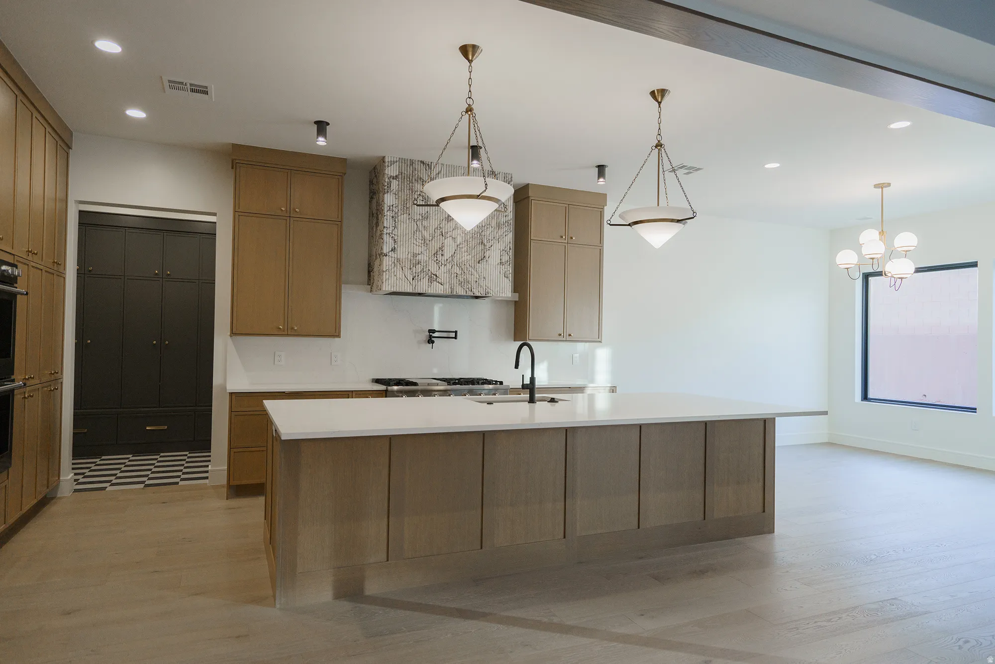 Open-concept kitchen featuring an expansive island, light wood-finish cabinetry, a striking stone range hood, and modern pendant lighting