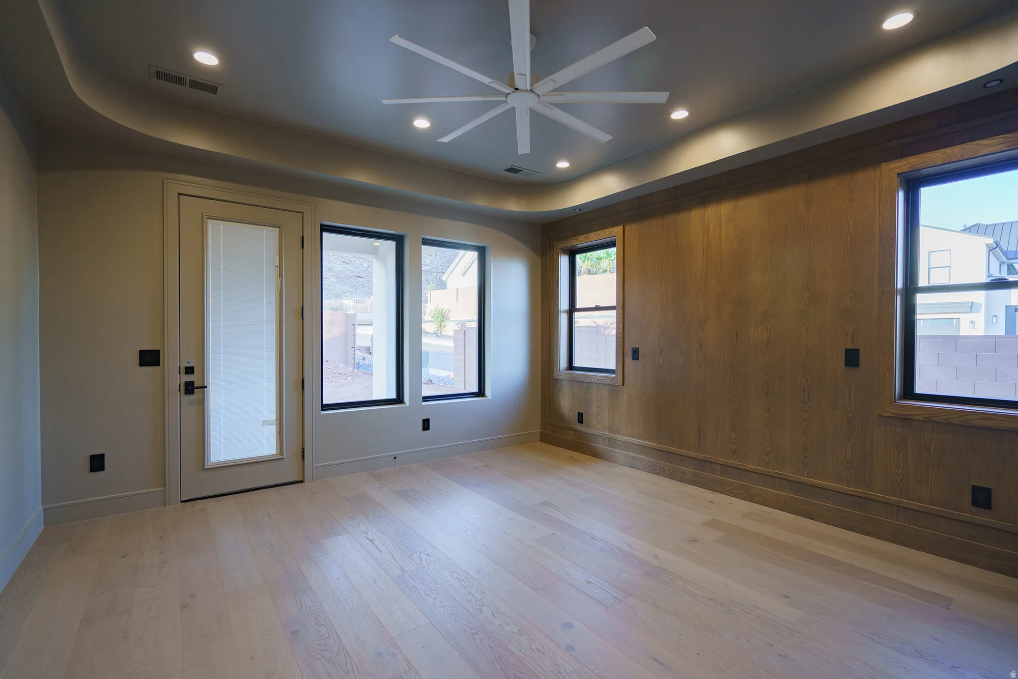 Recessed lighting, wood-finish flooring, accent wall with wood paneling, ceiling fan, and multiple windows