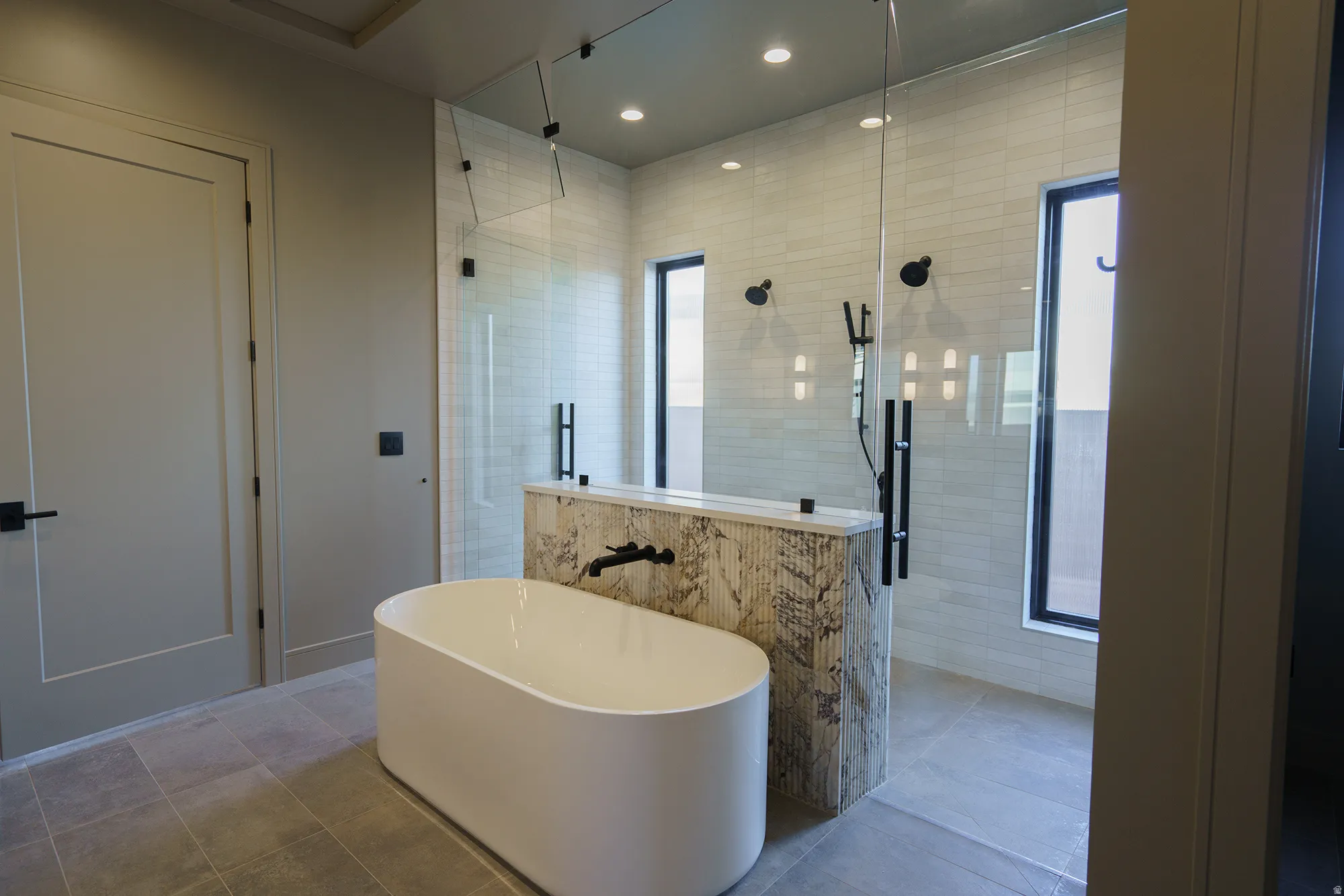 Freestanding soaking tub, large glass-enclosed shower, dual shower heads, tiled shower walls, and matte black fixtures