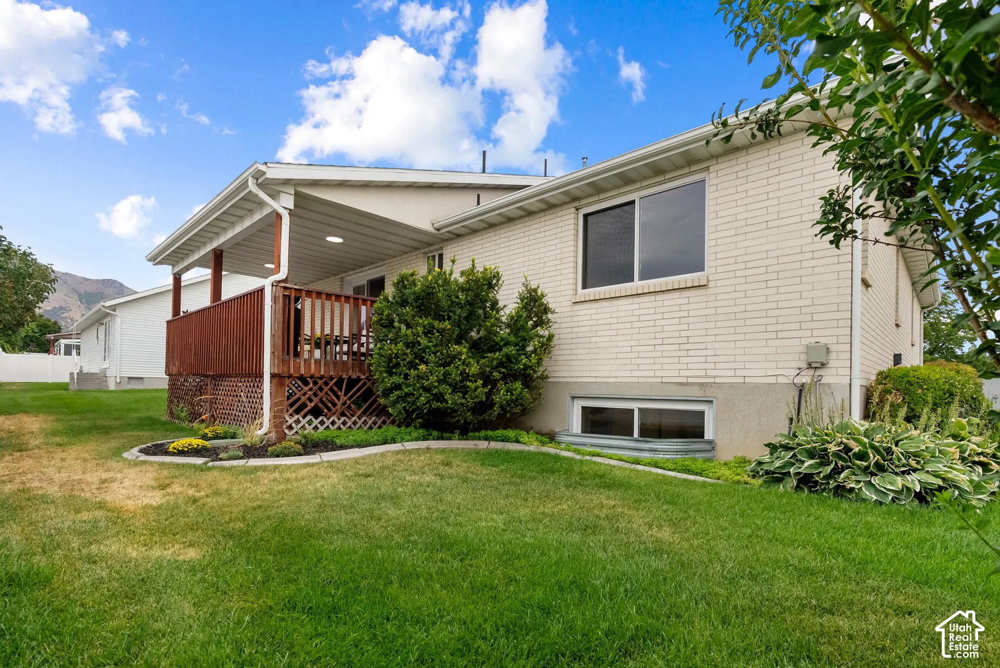 Expansive backyard featuring a covered patio with wood decking, brick exterior, and mature landscaping