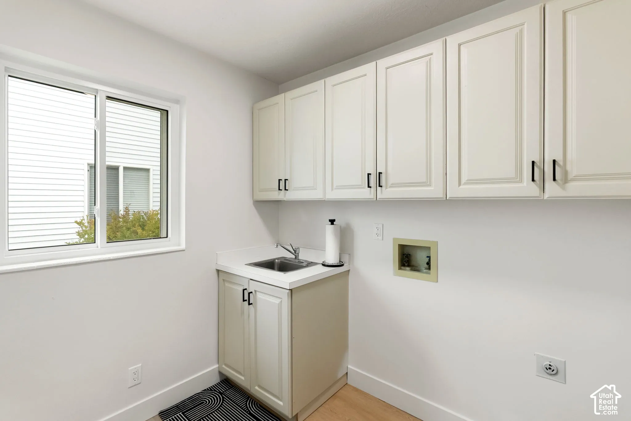 White cabinetry with black hardware, white countertop, stainless steel sink, and wood-finish flooring