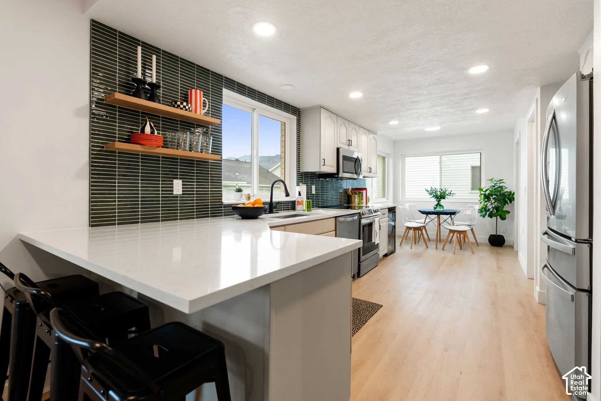 Kitchen with light wood-finish flooring, white cabinetry, a white countertop island, and dark rectangular tile backsplash