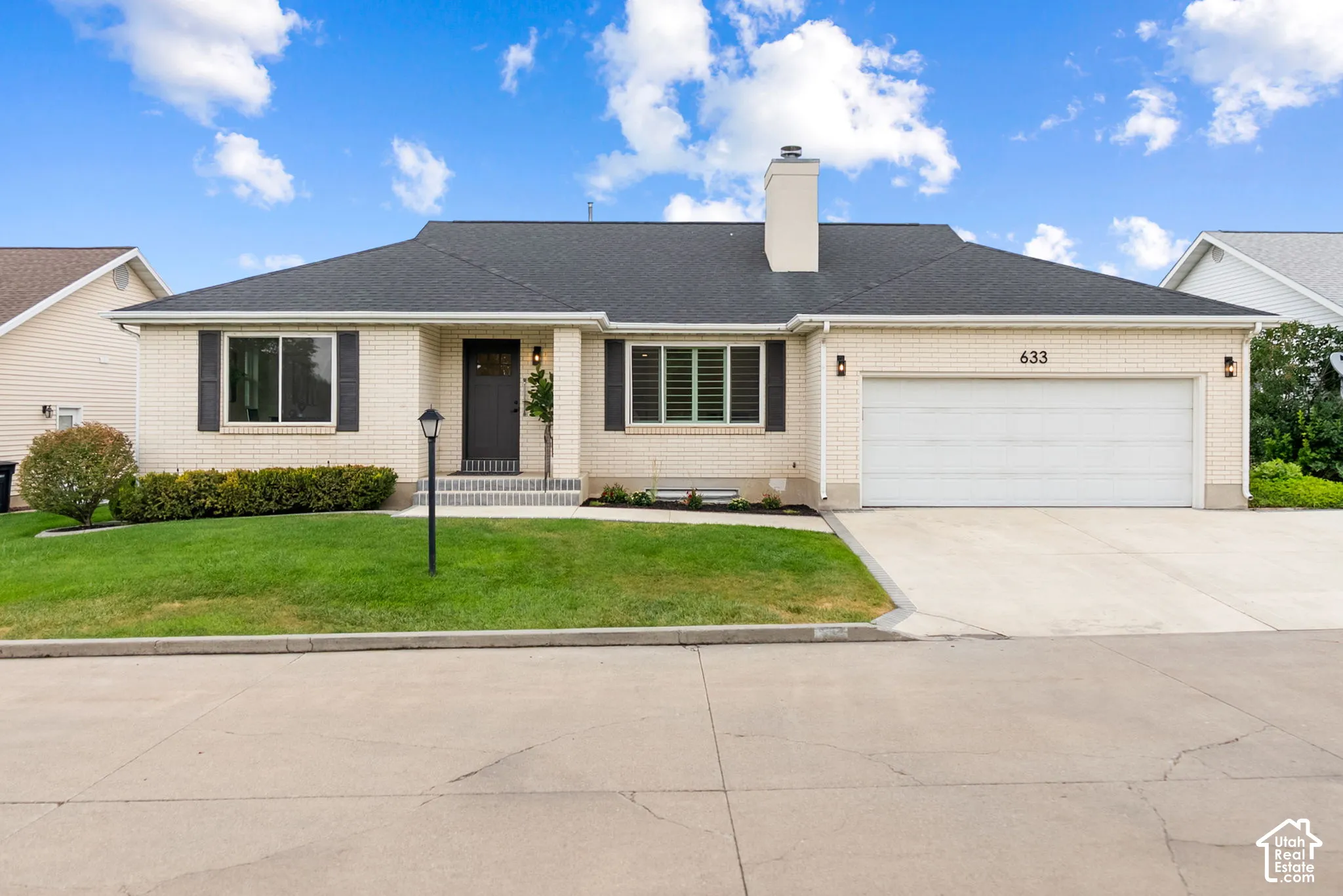 Cream brick exterior, dark asphalt shingle roof, attached two-car garage, front entry with dark door, and a concrete driveway