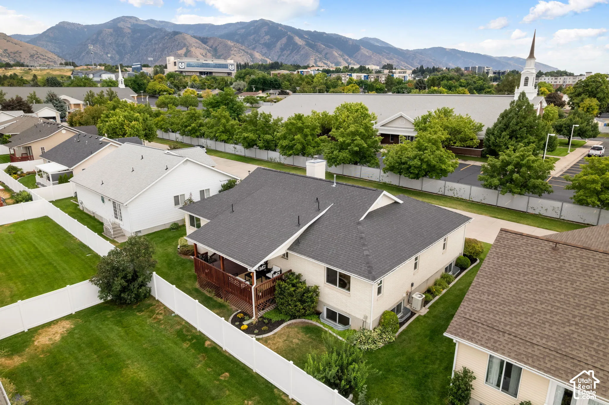 Expansive backyard featuring a white privacy fence, manicured lawn, and raised wood-finish deck