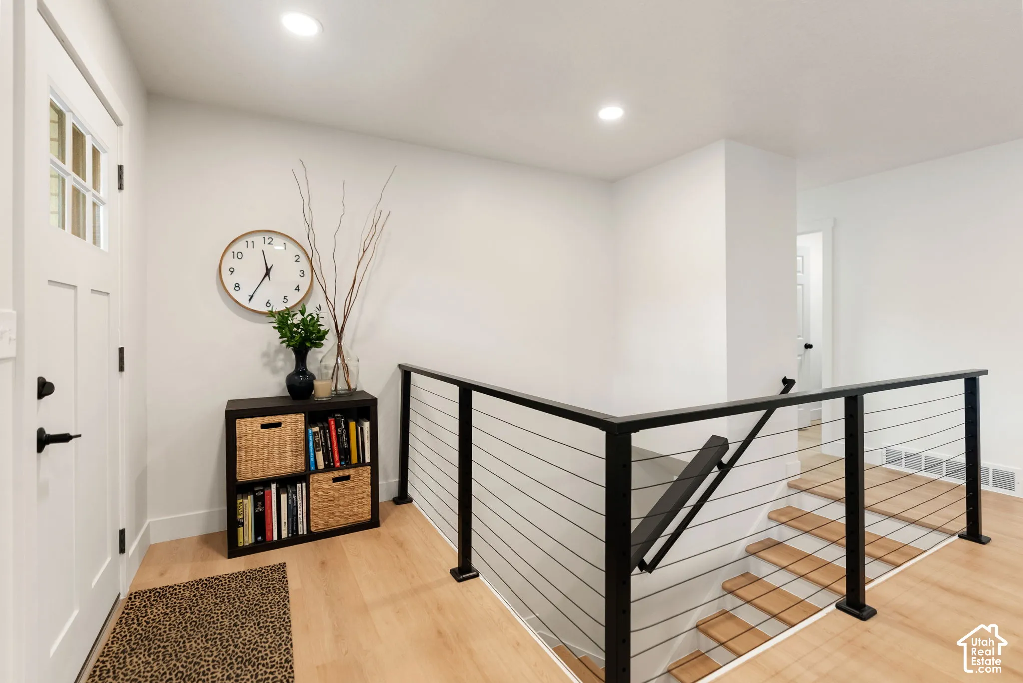 Modern cable railing system with a black finish, light wood-finish flooring, recessed lighting, and a paneled entry door with frosted glass