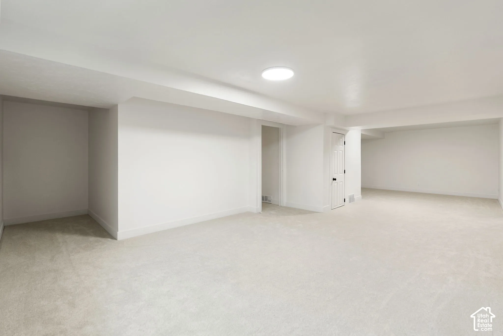 Expansive carpeted area with recessed lighting, a paneled door, and bright white walls