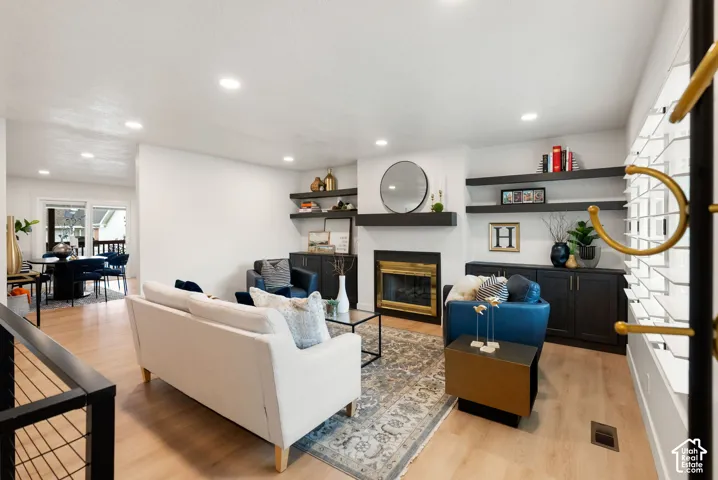 Living area with light-toned wood-finish flooring, recessed lighting, built-in shelving, fireplace with black surround, and built-in cabinetry
