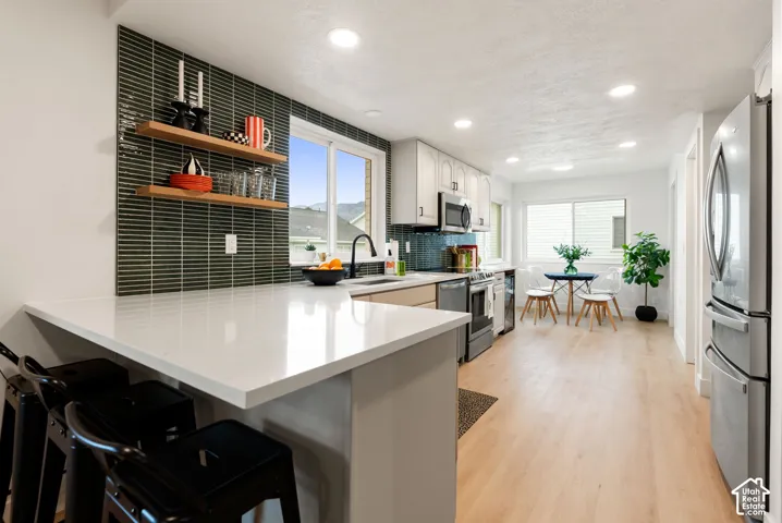 Kitchen with light wood-finish flooring, white cabinetry, a white countertop island, and dark rectangular tile backsplash