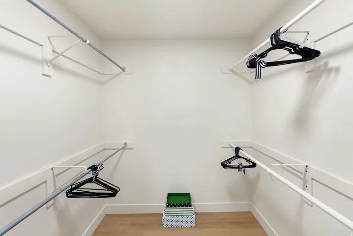 White walls, wood-finish flooring, and built-in closet rods with shelving