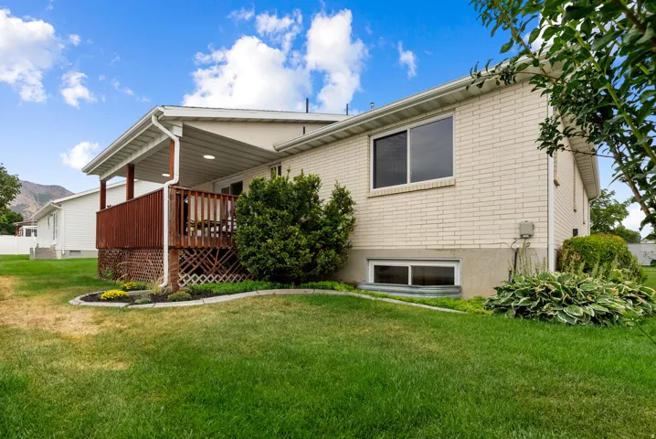 Covered wood deck with dark wood railing, white brick exterior, mature landscaping, and an expansive lawn