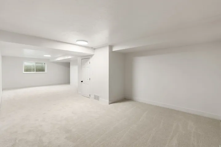 Expansive carpeted area with white walls, ceiling-mounted lighting, and a window with horizontal blinds