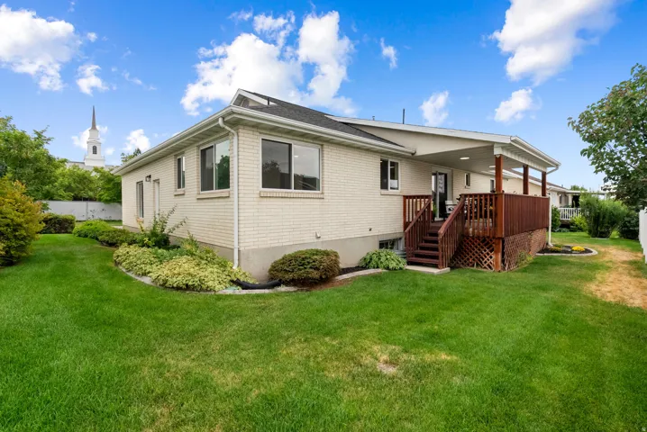 Brick exterior with white trim, covered wooden deck, mature landscaping, and a manicured lawn