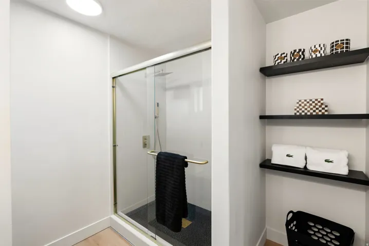 Glass-enclosed shower with gold-tone hardware, rainfall shower head, and mosaic tile flooring
