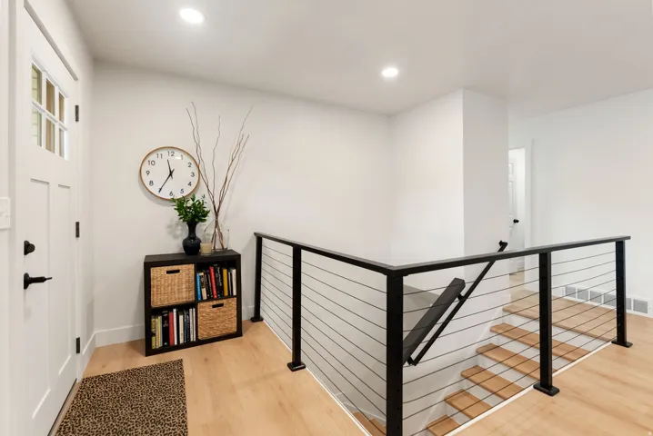 Modern cable railing system with a black finish, light wood-finish flooring, recessed lighting, and a paneled entry door with frosted glass