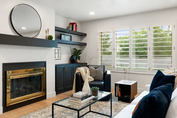 Fireplace with brass-finish trim, built-in cabinetry, floating shelves, window shutters, and wood-finish flooring